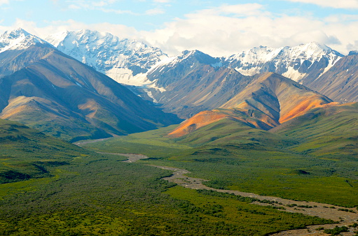 Photo of Polychrome Valley in Denali National Park, Alaska.  Panoramic picture shows several different geologic features including a valley, river running through the valley floor, snow capped mountains and starkly colored hills giving the valley its name