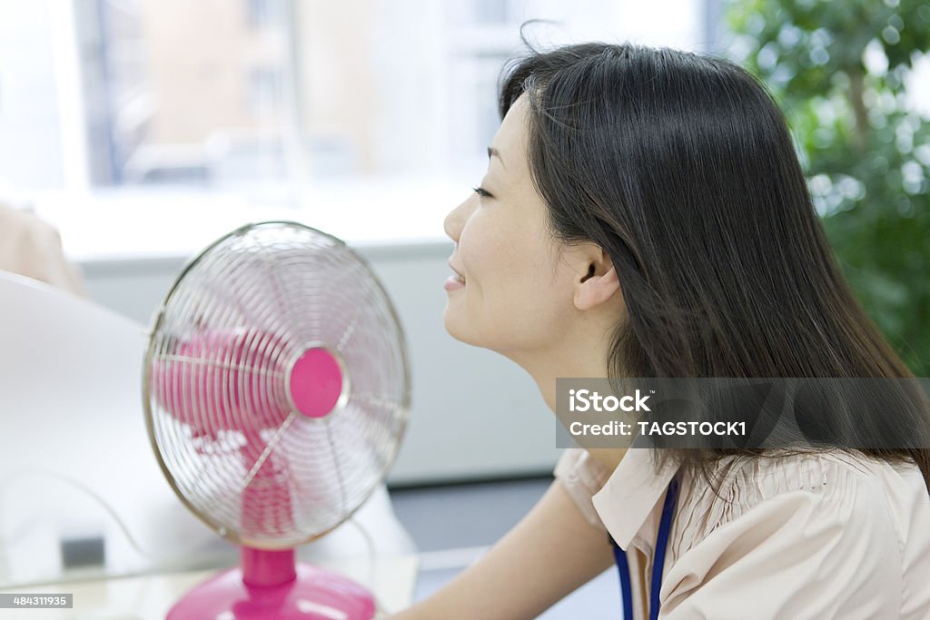 Woman sitting at desk with an electric fan Office Stock Photo