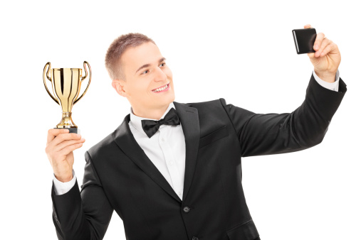 Elegant male holding a trophy and taking a selfie with phone isolated on white background