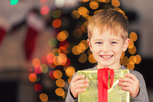 Happy young boy holding Christmas gift near decorated tree