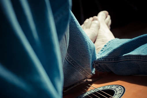 A mans legs wearing jeans, straddling an acoustic guitar.