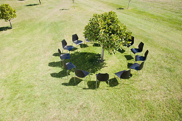 círculo de sillas de oficina alrededor de un árbol en campo - red chairs fotografías e imágenes de stock