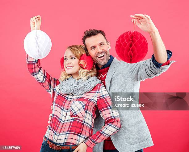 Happy Couple In Winter Outfit Against Red Background Holding Baubles Stock Photo - Download Image Now
