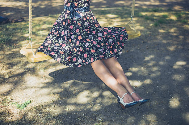 A young woman wearing a dress is sitting on a swing outside on a summer day