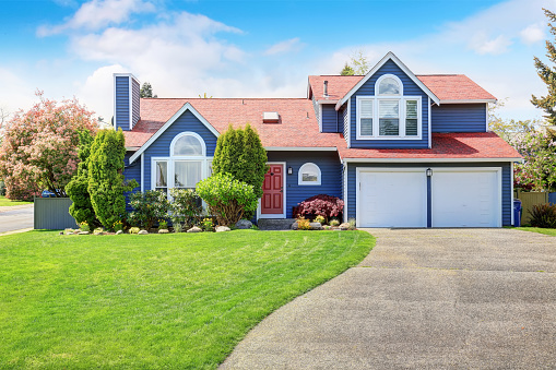 Large blue house with white trim, and well kept lawn, along with two garage spaces.