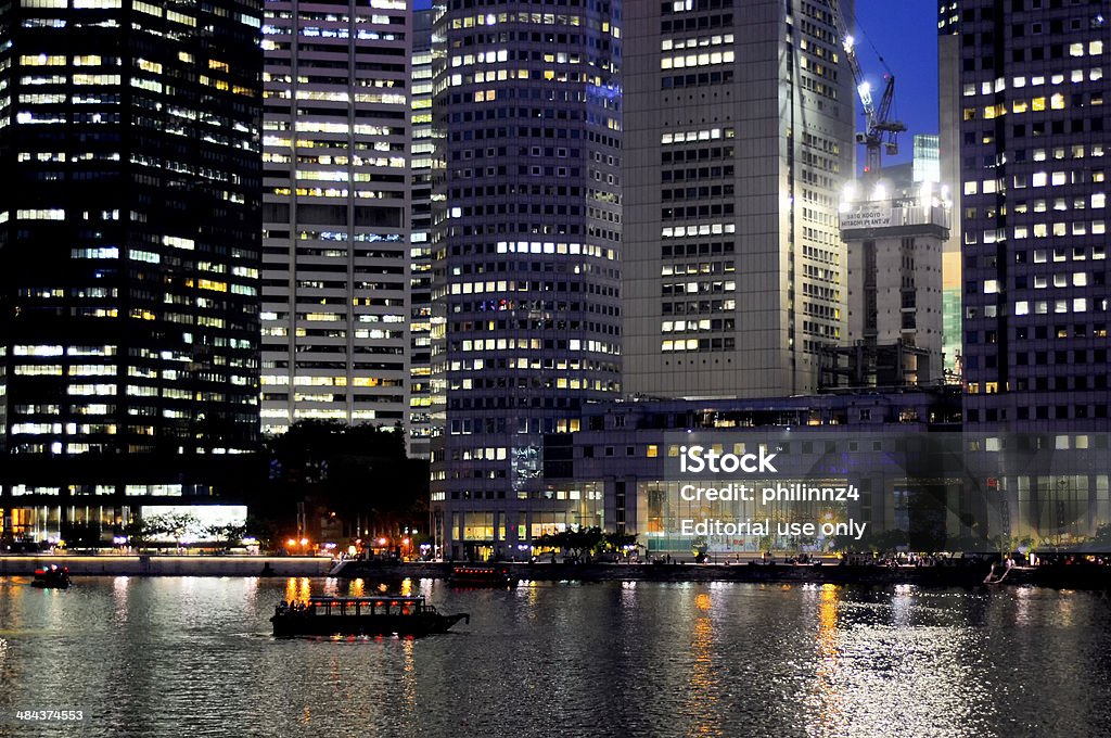 Singapore at night Singapore, Singapore - July 9, 2010: nighttime in Singapore showing the lights and sights, in particular the river with a small cruise boat and on the other side some highrise buildiings partly lit up Apartment Stock Photo