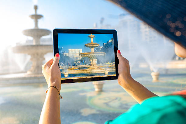 Young female traveler photographing with digital tablet central fountain in Bucharest city, Romania