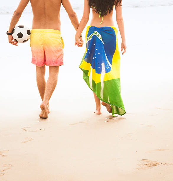 Young couple walking along beach with football and Brazil Flag stock photo