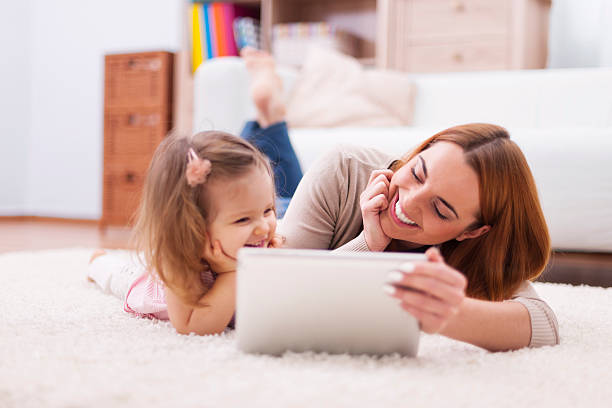 linda niña con mamá usando tableta digital en su hogar - playing playful baby contemporary fotografías e imágenes de stock
