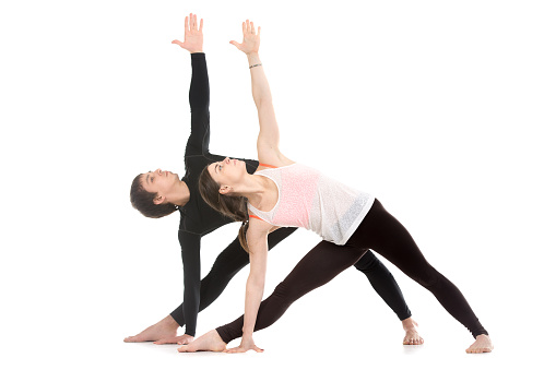 Two sporty people practice yoga with partner, couple doing stretching exercise, extended triangle pose, utthita trikonasana