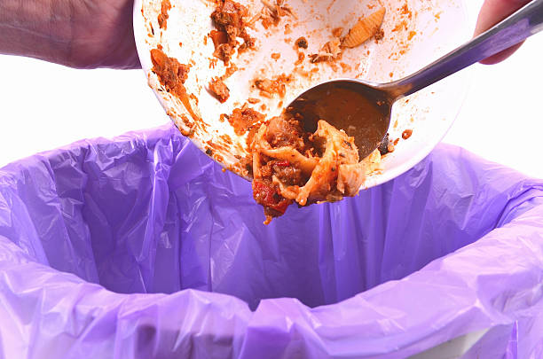 Scraping leftover food from a bowl into a garbage bag A person removes leftover food into a bin scraping stock pictures, royalty-free photos & images