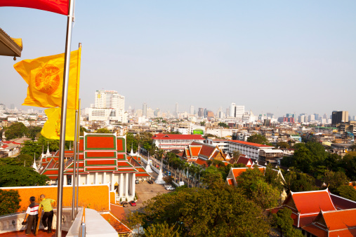 Bangkok, Thailand - February, 19th 2013: Bangkok seen from Wat Saket, taken is taen from way and steps up to temple. At left side are some Thai flags. Two Thai men are walking down. One man is using crutch.