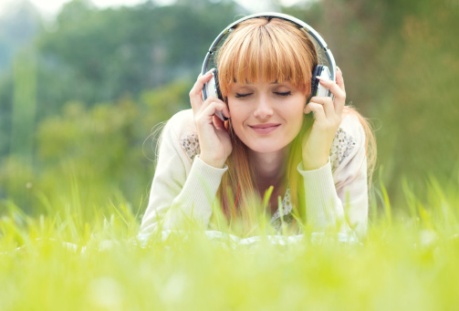 Beautiful young woman with headphones. Enjoy music outdoors. Girl repose or lie down