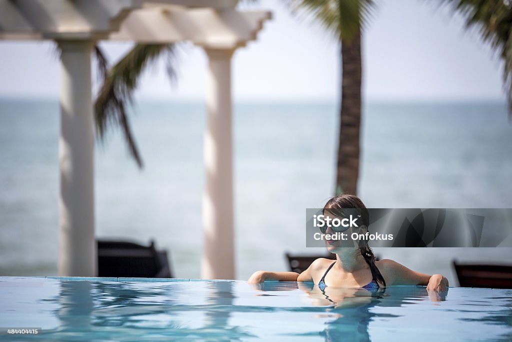 Woman Relaxing Inside Infinity Pool At Tropical Resort Woman Relaxing Inside Infinity Pool At Tropical Resort in Vietnam. There is some palm trees and the sea in the background o this beautiful sunny day. Active Lifestyle Stock Photo