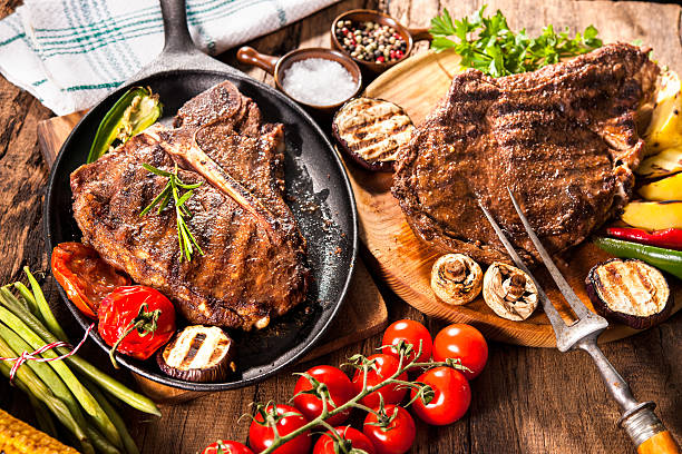 Beef steaks with grilled vegetables Beef steaks with grilled vegetables and seasoning on wooden background t bone steak stock pictures, royalty-free photos & images