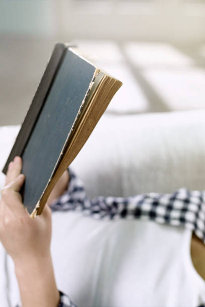 istock Young woman on sofa reading a book 484408362