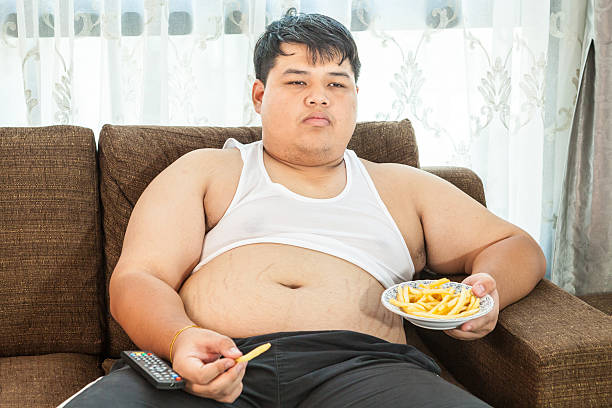 gordo preguiçoso homem sentado com comida rápida - remote fat overweight dieting imagens e fotografias de stock