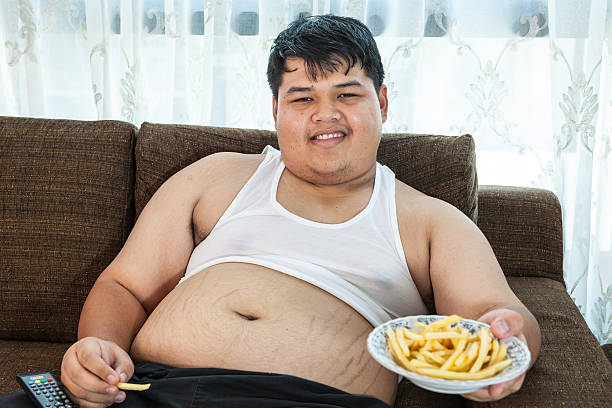 gordo preguiçoso homem sentado com comida rápida - remote fat overweight dieting imagens e fotografias de stock