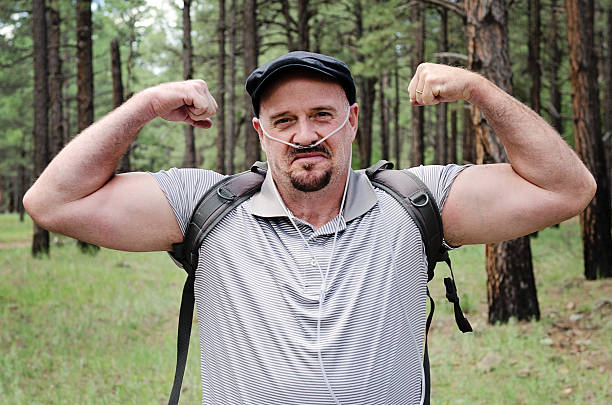 Strong Patient Middle aged man flexes his muscles as he hikes in the woods wearing therapeutic oxygen. disabled person hiking outdoors stock pictures, royalty-free photos & images