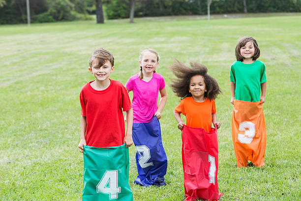 Color photo of a group excited boys and girls having a potato sack race against each other in the grass outside on a beautiful summer day.