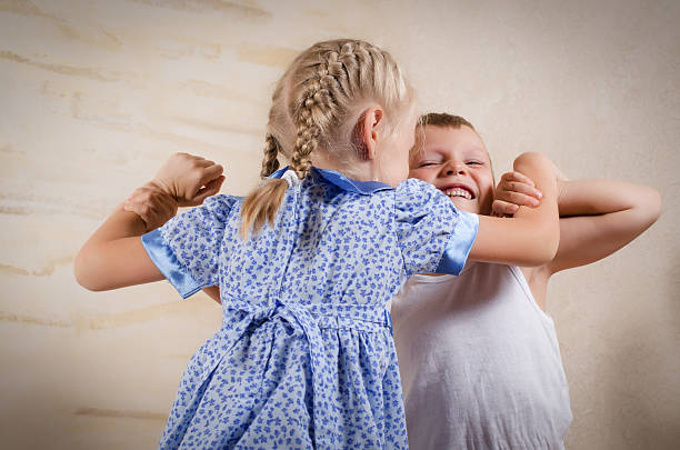 Small girl with her blond hair in pigtails fighting with a young boy who is grimacing in anger as they wrestle together with their arms locked