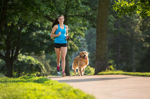 A female jogger and a golden retriever running on a paved trail.