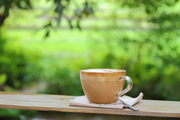 Hot coffee cup resting on a wooden board in nature.