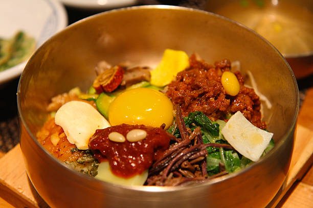 Traditional Korean dish of mixed rice with vegetables and egg in a hot stone pot, served in a golden bowl.