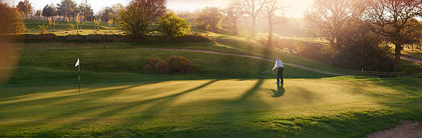 leuchtendes golfplatz mit golfspieler auf dem putting green - golf golf flag sunset flag stock-fotos und bilder