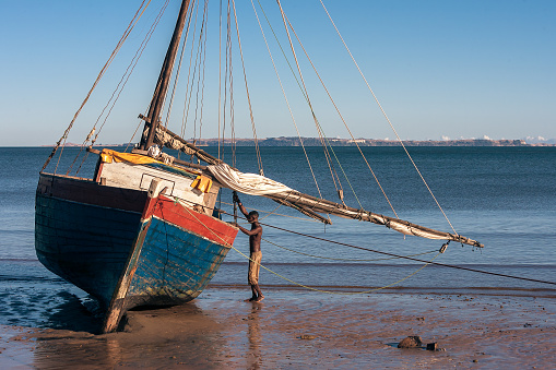 Analalava, Madagascar - June 27, 2010:  Malagasy boatman and his schooner beached at low tide near Analalava, west of Madagascar.