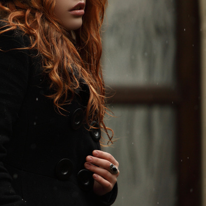 Beautiful young woman with long red hair in winter clothes In black beret against the background of an old building