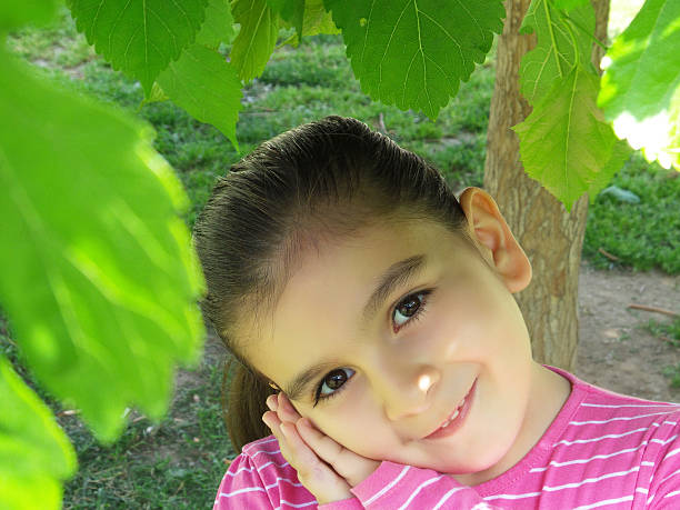 A young girl is sitting on a pink rug during a picnic, with a white basket of fruit standing nearby. A seductive girl in a floral dress is holding a red apple in her hands. The lady creates an atmosphere of tenderness and comfort on a summer day at a picnic.