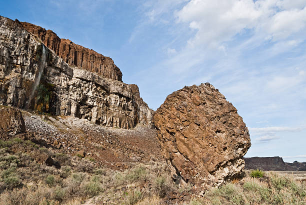 Giant Basalt Boulder at the Base of a Cliff East of the Cascade Mountains, Washington’s climate is arid and the terrain is desert-like. Summertime temperatures can exceed 100 degrees Fahrenheit in regions such as the Yakima Valley and the Columbia River Plateau. This is an area of rolling hills and flatlands. During the last Ice Age, 18,000 to 13,000 years ago, floods flowed across this land, causing massive erosion and leaving carved basalt canyons, waterfalls and coulees known as the Channeled Scablands. The Quincy Lakes area is part of the scablands of central Washington State. Visitors to this area will experience basalt cliffs, mesas, benches, canyons and potholes. Several of the potholes have become lakes that are filled with water seeping from the irrigation of nearby upslope farmlands. Ancient and Dusty lakes are two examples that have added to fish and wildlife diversity and have also become important recreational areas. Ancient Lake and Dusty Lake are in the Quincy Wildlife Recreation Area near Quincy, Washington State, USA. jeff goulden washington state desert stock pictures, royalty-free photos & images