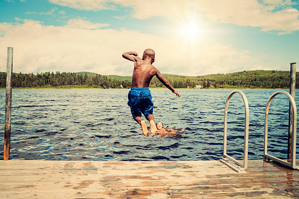 Young african-american boy jumping from a pier in lake.