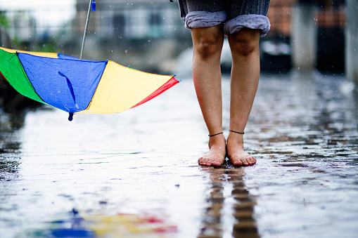 Woman legs in rain with multi-colored umbrella