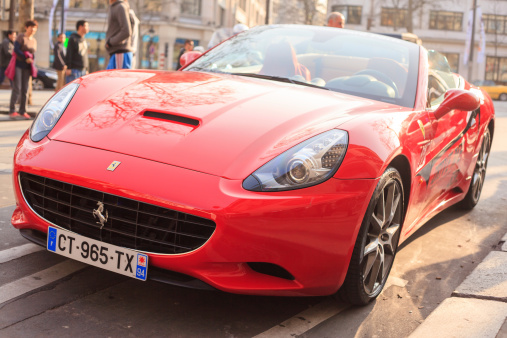Paris, France - March 13, 2014: A red Ferrari California sits in Paris, France. The high performance, exotic, sports car can be seen parked along the street in Paris, France.  The Ferrari was parked along the Avenue des Champs-Élysée, while people can be seen standing in the background