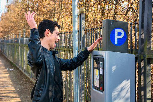 Young man angry at parking ticket to be dispensed from the ticket booth at the side of a street after making his payment