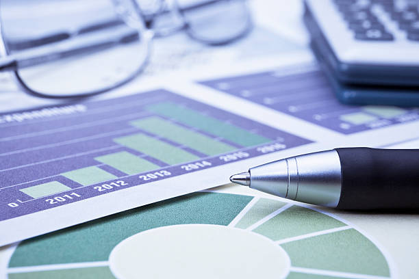 Closeup of black pen, calculator, eye glasses and financial charts stock photo