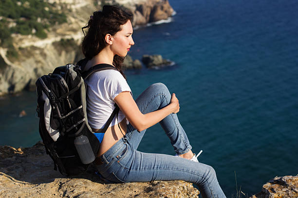 istock Pretty girl traveler is sitting on rock edge with backpack 484486548