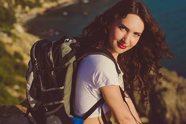 istock Happy girl with backpack is sitting on rock peak 484486574