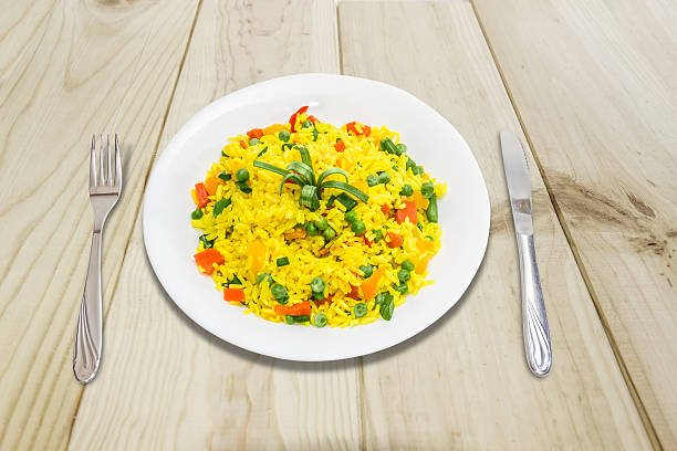 Boiled rice with vegetables White dish with boiled rice, cooked with turmeric, with boiled vegetables - carrots, bell peppers, green peas, green beans, fork and knife on a wooden surface. knif stock pictures, royalty-free photos & images