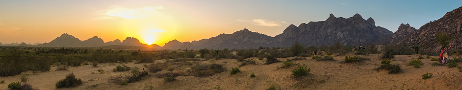 Panorama of desert scene with mountain range in sunset with people in distance.