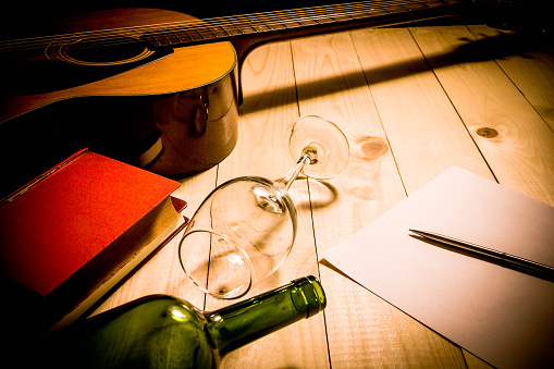 Guitar with Red Book and Wine on a wooden table.