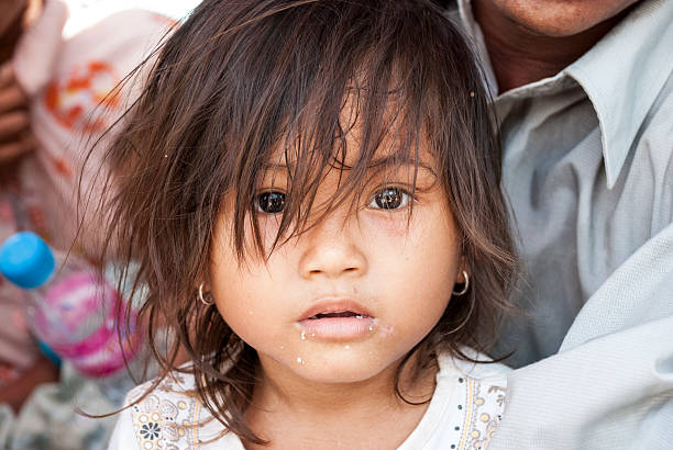 Phnom Penh, Cambodia - June 19, 2007: A Cambodian girl sits in her father's lap while waiting in a long line outside a clinic for free child vaccinations in Phnom Penh, Cambodia