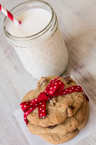 Chocolate chip cookies tied with red ribbon with a glass of milk