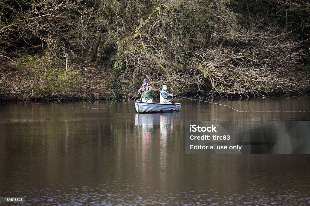Two fly fishermen in a boat at the lake Llanelli, Wales - April 9, 2014: Side view of two middle-aged caucasian fly fishermen sitting in a rowing boat using their fishing rods for trout fishing at the lake. The location is the Llanelli Town Reservoir in the Welsh countryside Adult Stock Photo