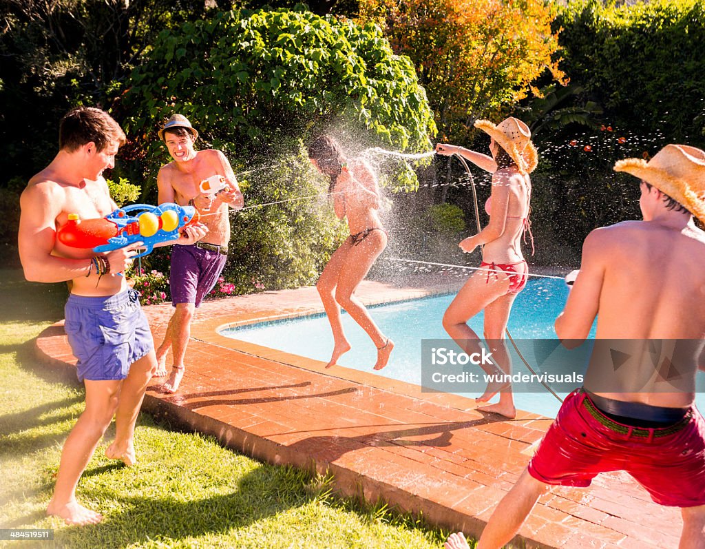Group of friends playing with water guns Group of happy friends playing with water guns by swimming pool Squirt Gun Stock Photo