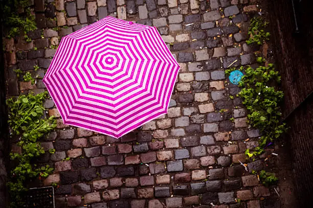 Unrecognizable female under umbrella walking on paved street