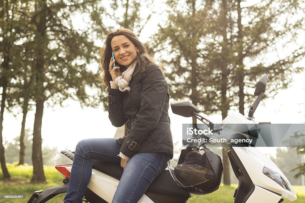 Woman outdoors leaning on scooter holding her mobile phone Woman outdoors leaning on scooter holding her mobile phone. Adult Stock Photo