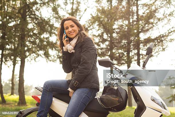 Woman Outdoors Leaning On Scooter Holding Her Mobile Phone Stock Photo - Download Image Now